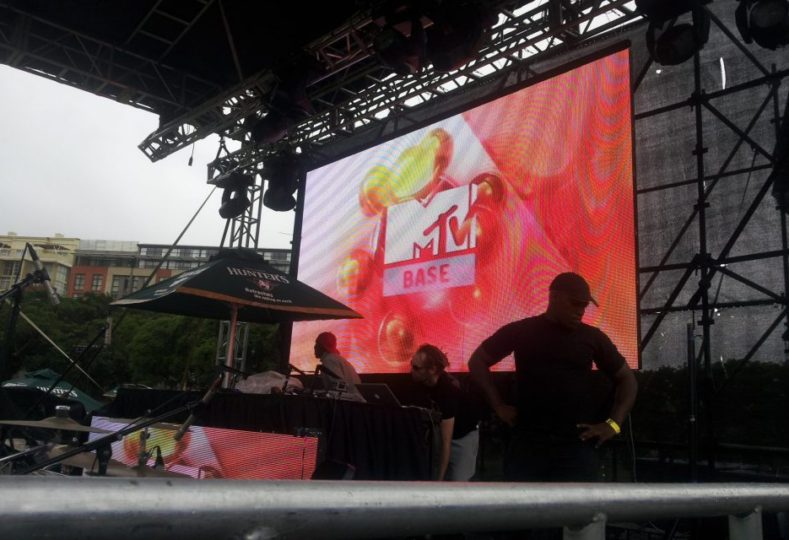 Image shows a large outdoor screen above a live music stage