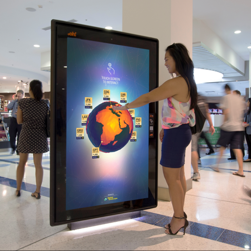 Image shows a young woman interacting with a digital touch screen