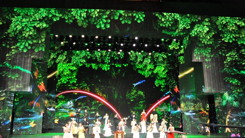 Image shows large screens showing trees and leaves as the backdrop to a stage production