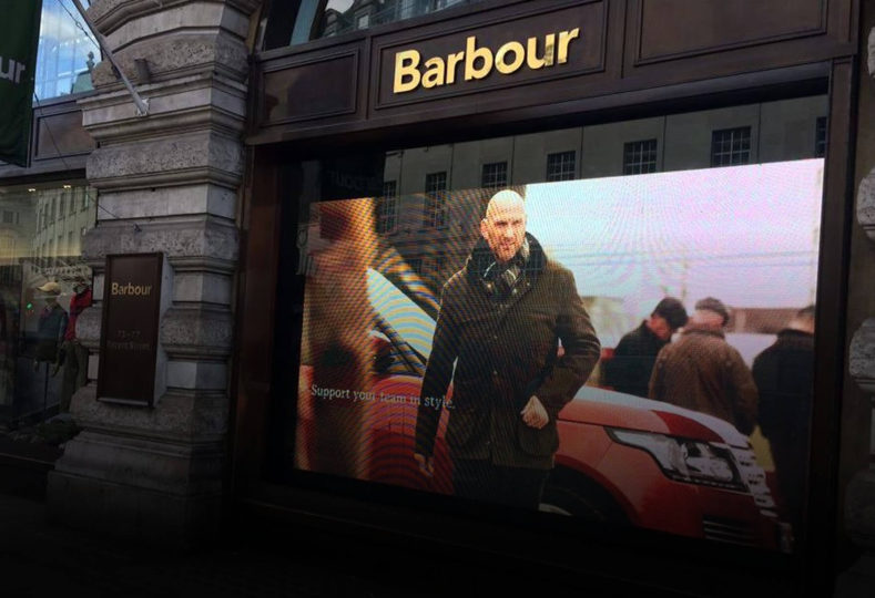 Image shows a digital screen in the window of a Barbour store